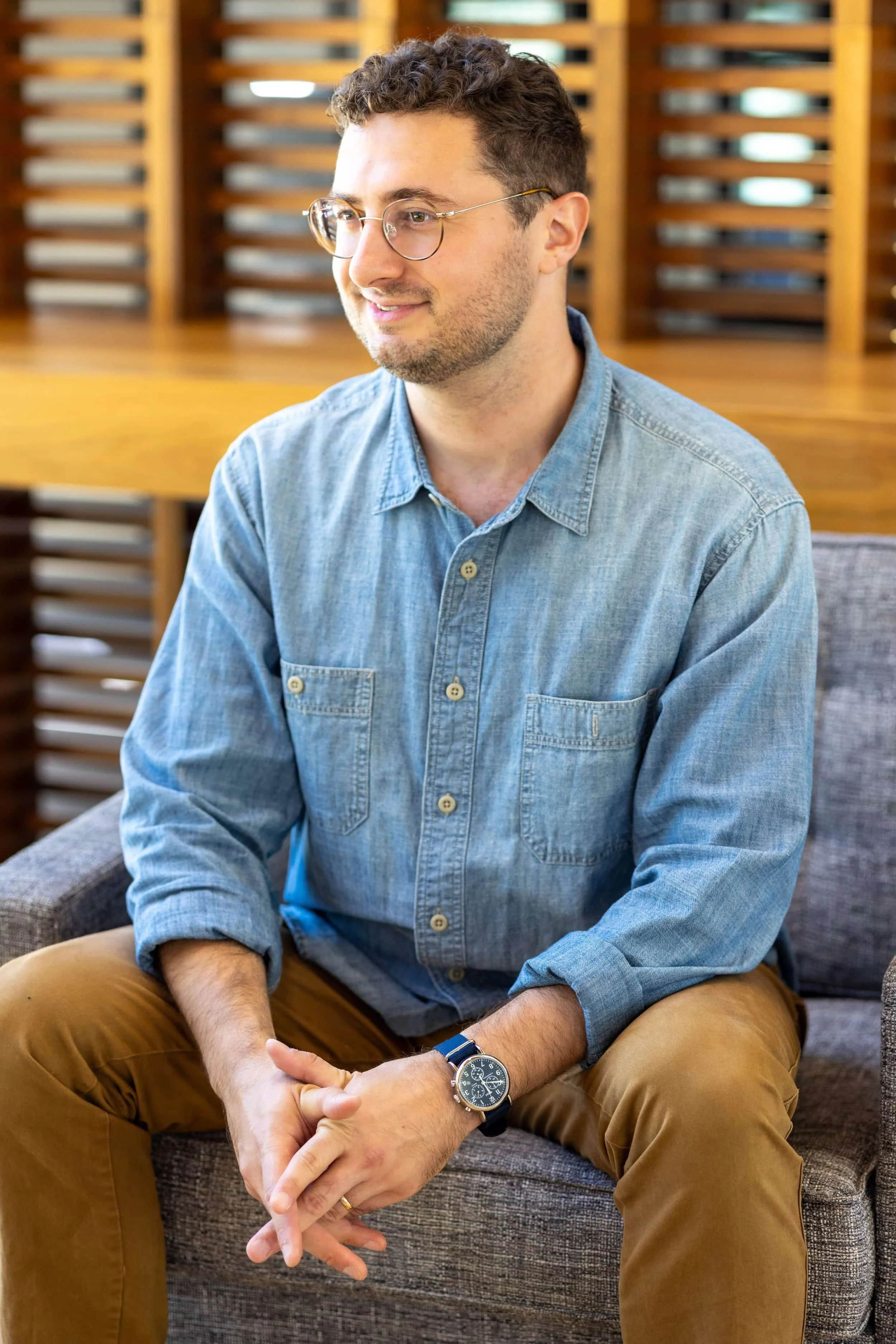 A trauma therapist in glasses and a denim shirt sits on a gray chair, smiling warmly—just the setting for attachment therapy.A man in glasses and a denim shirt sits on a gray chair, smiling warmly—just the setting for attachment therapy.