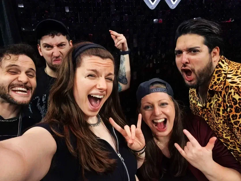 Group of five friends taking a selfie together, making silly faces and gestures in a party or club setting.