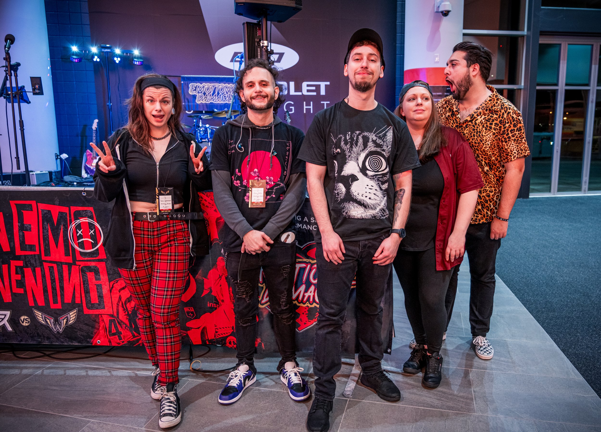 Group of five young adults posing together at a music event with a stage and band setup in the background.