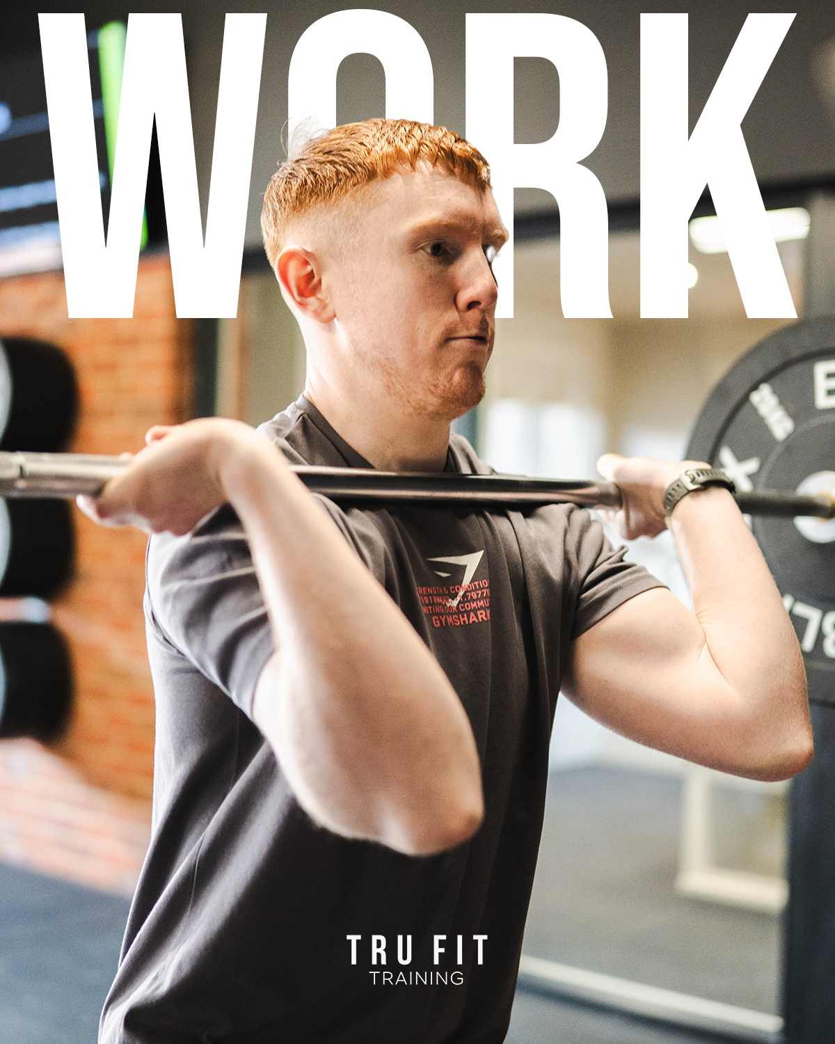 A young man with red hair and a focused expression lifts a barbell across his shoulders in a gym, with the words 'WORK' overlayed across the top of the image and 'TRU FIT TRAINING' at the bottom.