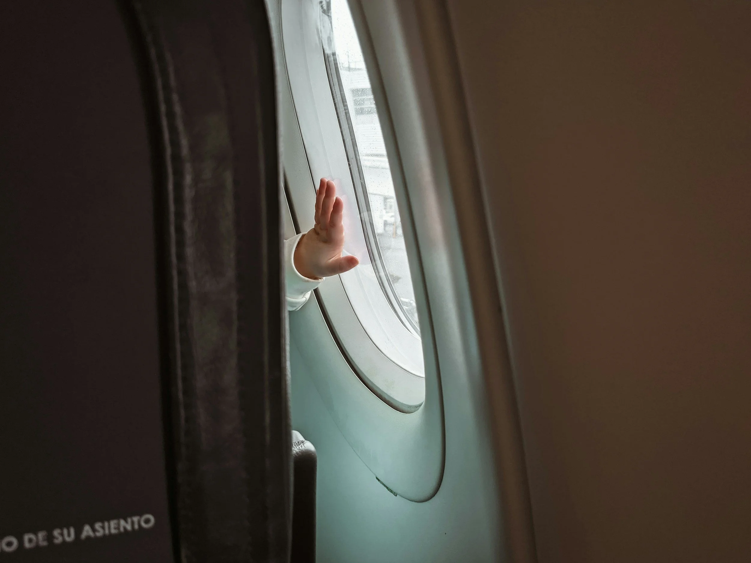 A baby's hand on the window of an airplane featured in a blog about how to travel with a baby on a plane.