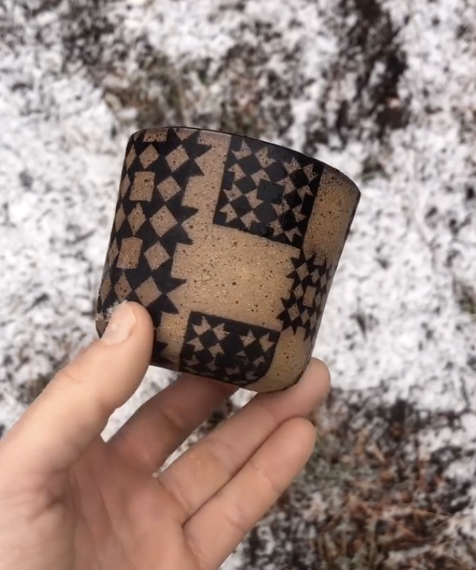 Hand holding a ceramic mug with geometric star patterns, outdoors on snow-covered ground.