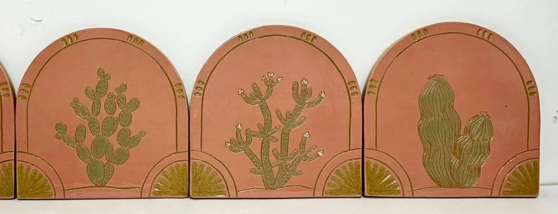 Decorative tiles with gold cactus plant designs in various shapes on a pink background.