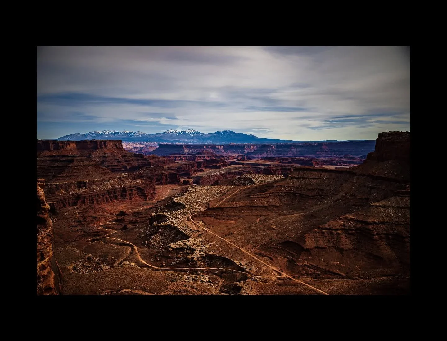 From the Island in the Sky mesa in Canyonlands National Park, the Colorado Plateau unfolds in layers of Permian and Triassic sandstone &mdash; canyon walls, buttes, and switchbacking four-wheel-drive tracks cutting across the canyon floor below. The 
