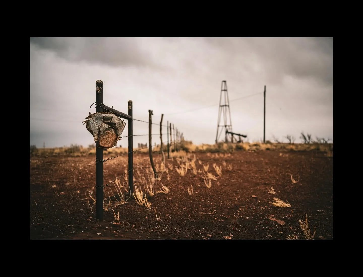 A weathered fence stretches toward a lone pumpjack beneath a low, unsettled sky. In the high desert, industry and open range share the same horizon&mdash;steel and sagebrush bound to the same wind.

#WesternLandscapes #EnergyAndLand #HighDesert #Rura