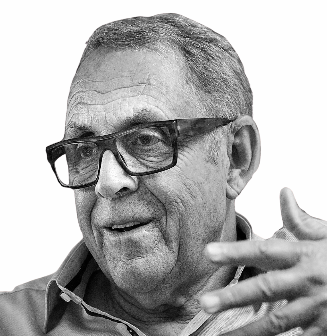 A black and white close-up of an elderly man with glasses, speaking and gesturing with his hand.