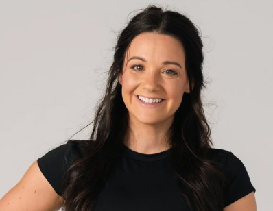 A young woman with long dark hair smiling at the camera, wearing a black t-shirt against a light gray background.