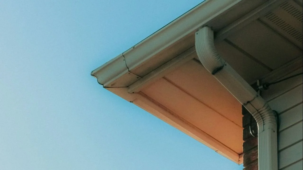 Residential roofline with a white gutter and downspout.