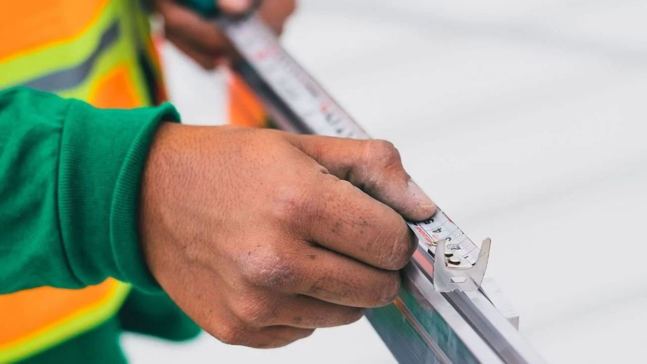 Worker using a measuring tape to measure gutter material for proper installation. 