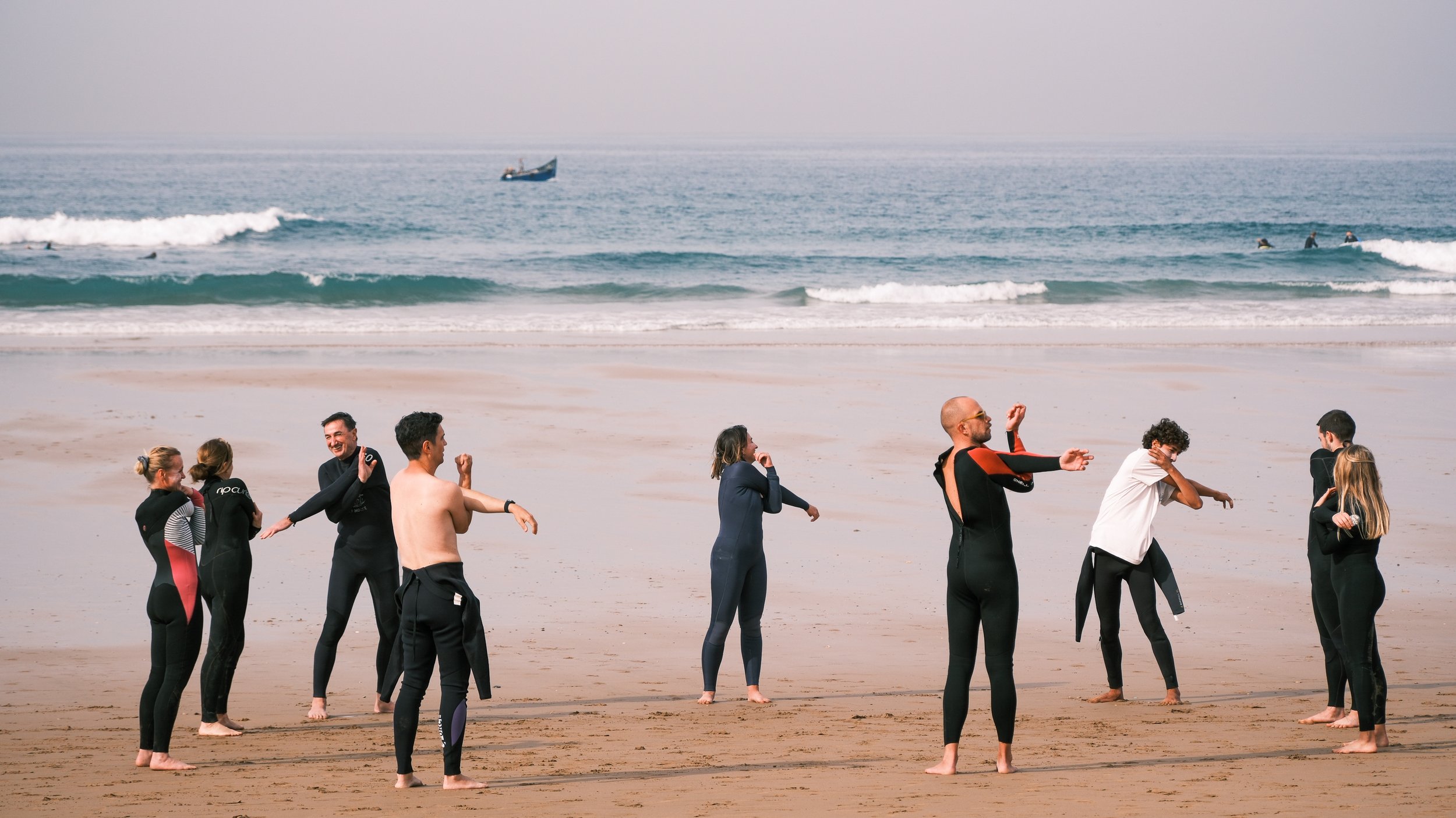 Group of people in wetsuits stretching on a beach near the ocean.