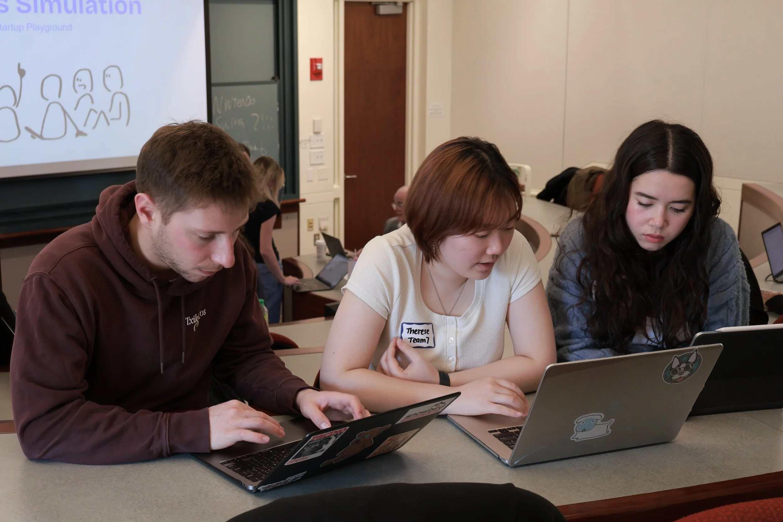 Boston University students collaborating on laptops during a SimBus in-class business simulation.