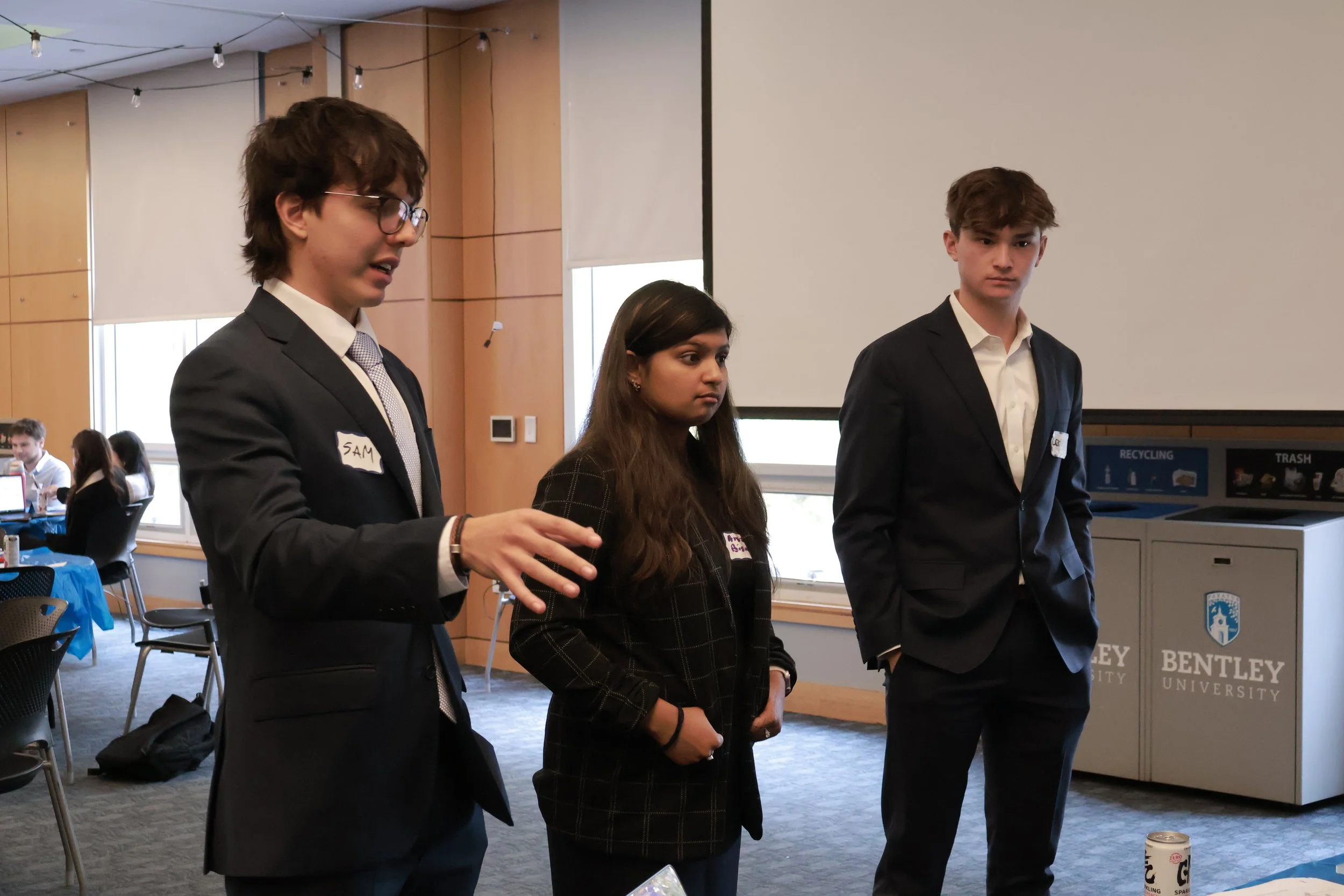 Bentley University student entrepreneurs in business attire delivering a pitch during the SimBus Founders' Hustle Day experiential learning simulation.