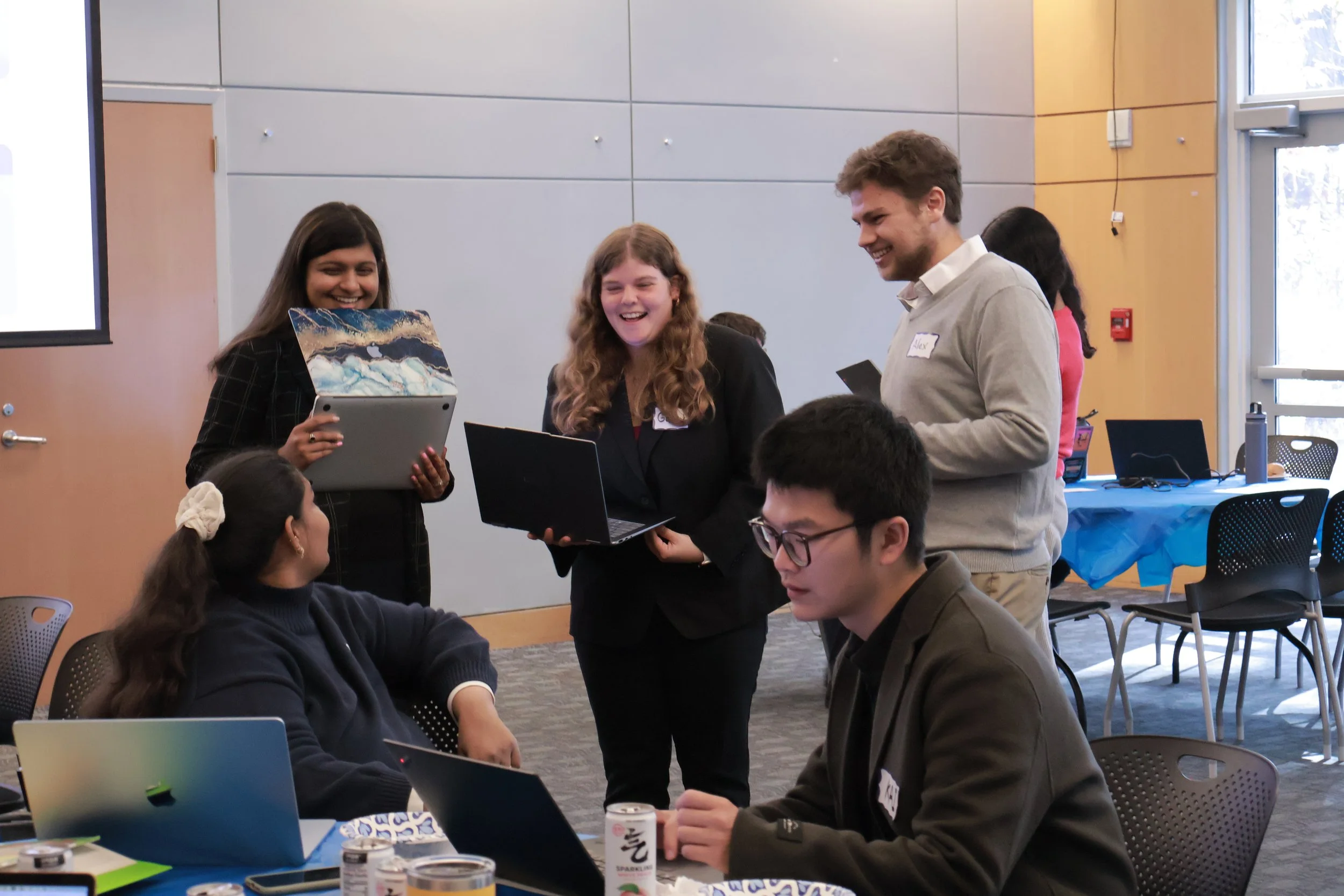 Student entrepreneurs smiling and engaging in team collaboration with laptops at a live SimBus business simulation workshop.