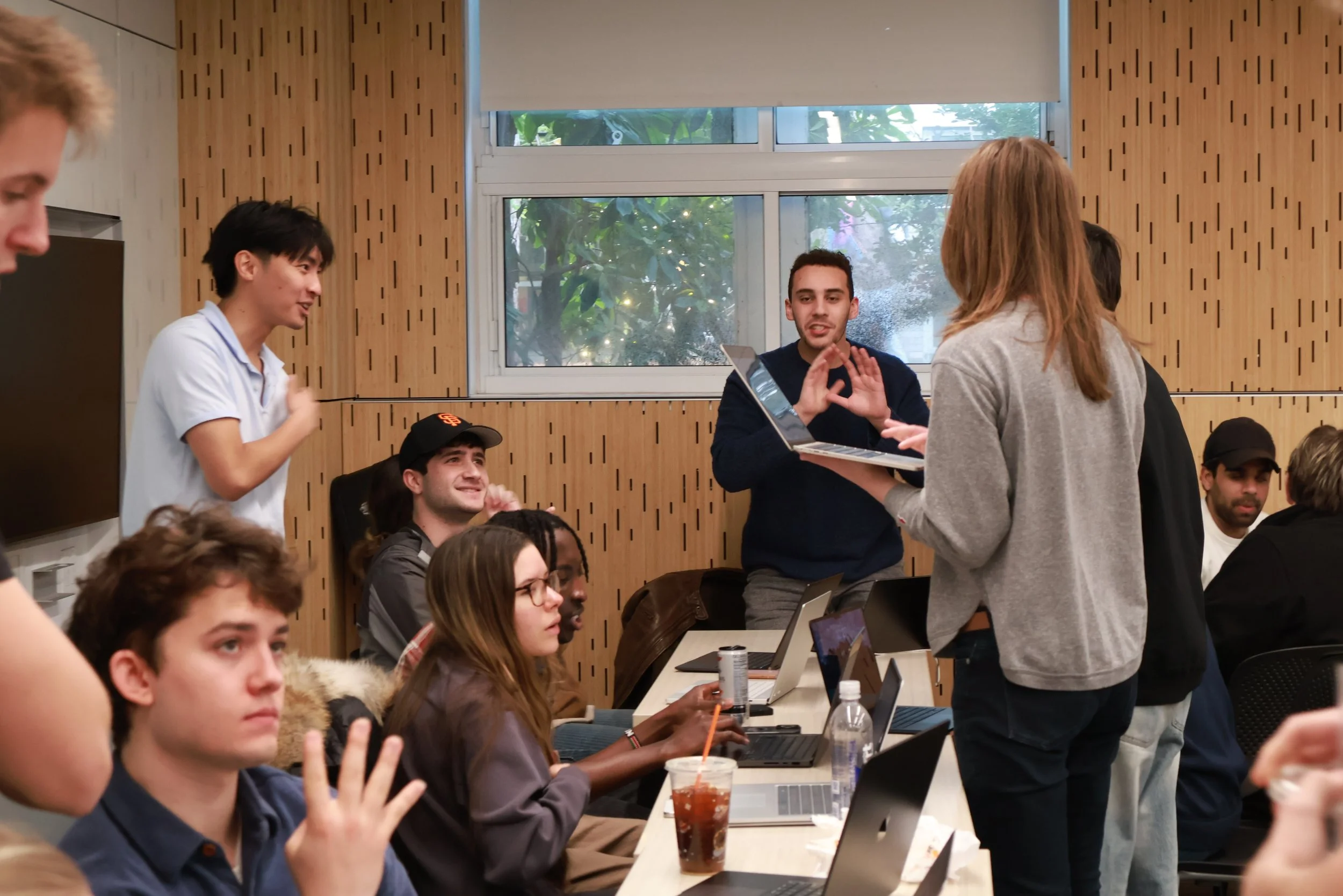 A dynamic and high-energy classroom scene of college students actively discussing market tactics and sharing ideas on laptops during a live SimBus Simulation at a entrepreneurship class.