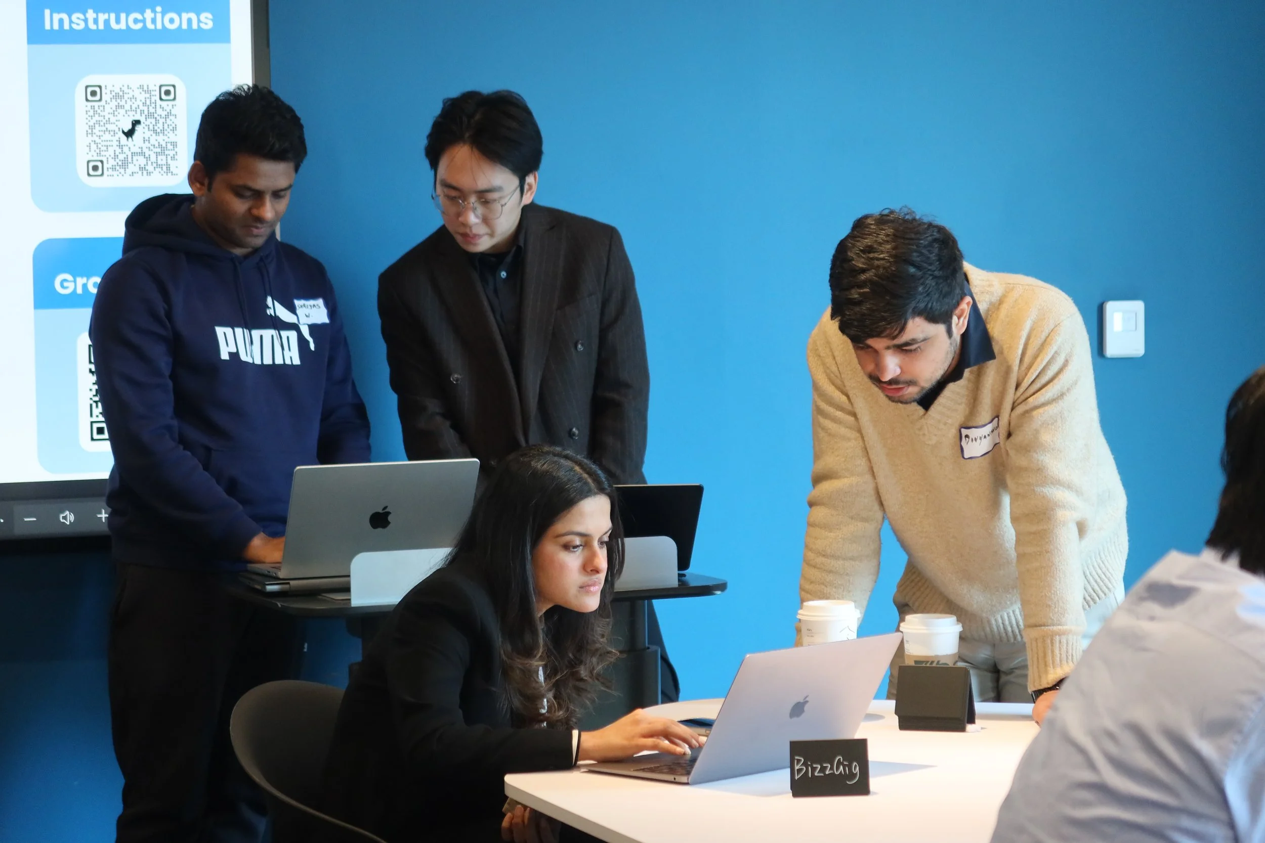 Northeastern University students collaborating on startup strategy around a laptop during the SimBus Game of Ventures experiential learning simulation.