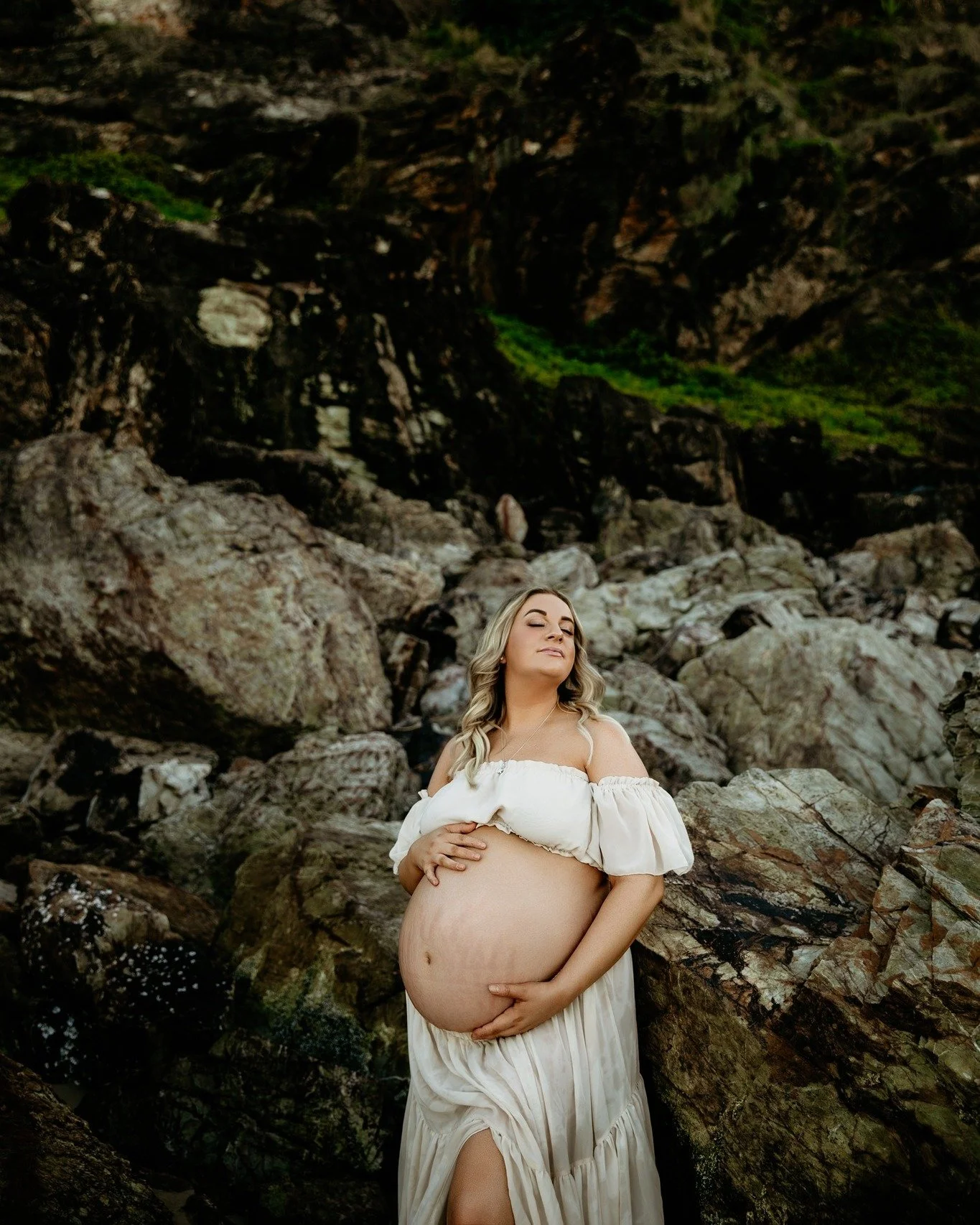 She leans into the earth, carrying life with both strength and softness 🌙✨

In colour, you feel the warmth &mdash; the glow of skin, the golden light, the gentle cream of her gown against rugged stone.
In black &amp; white, you feel the essence &mda