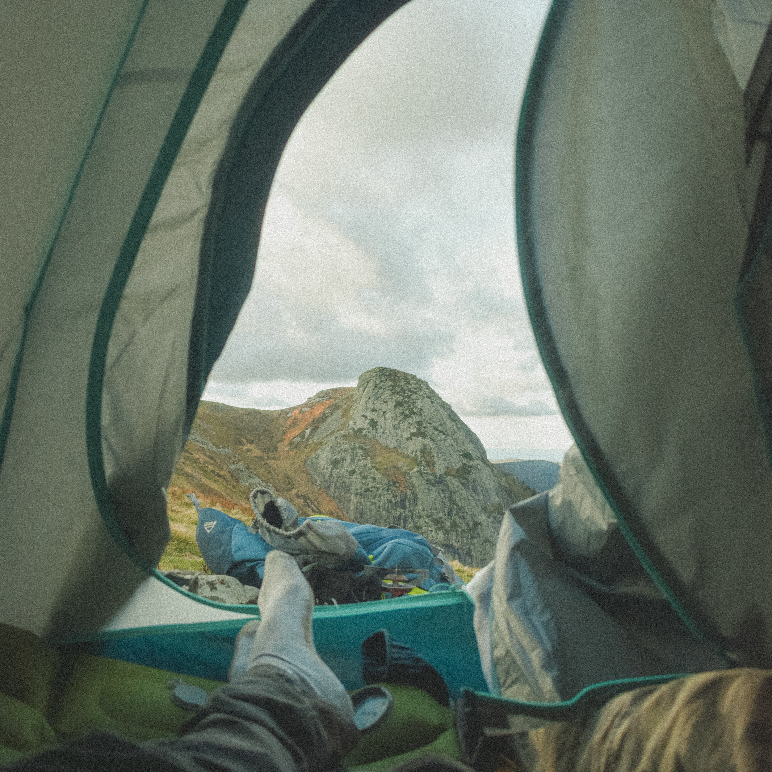Vue depuis l'intérieur d'une tente montrant un paysage de montagne avec un sommet rocheux sous un ciel nuageux.