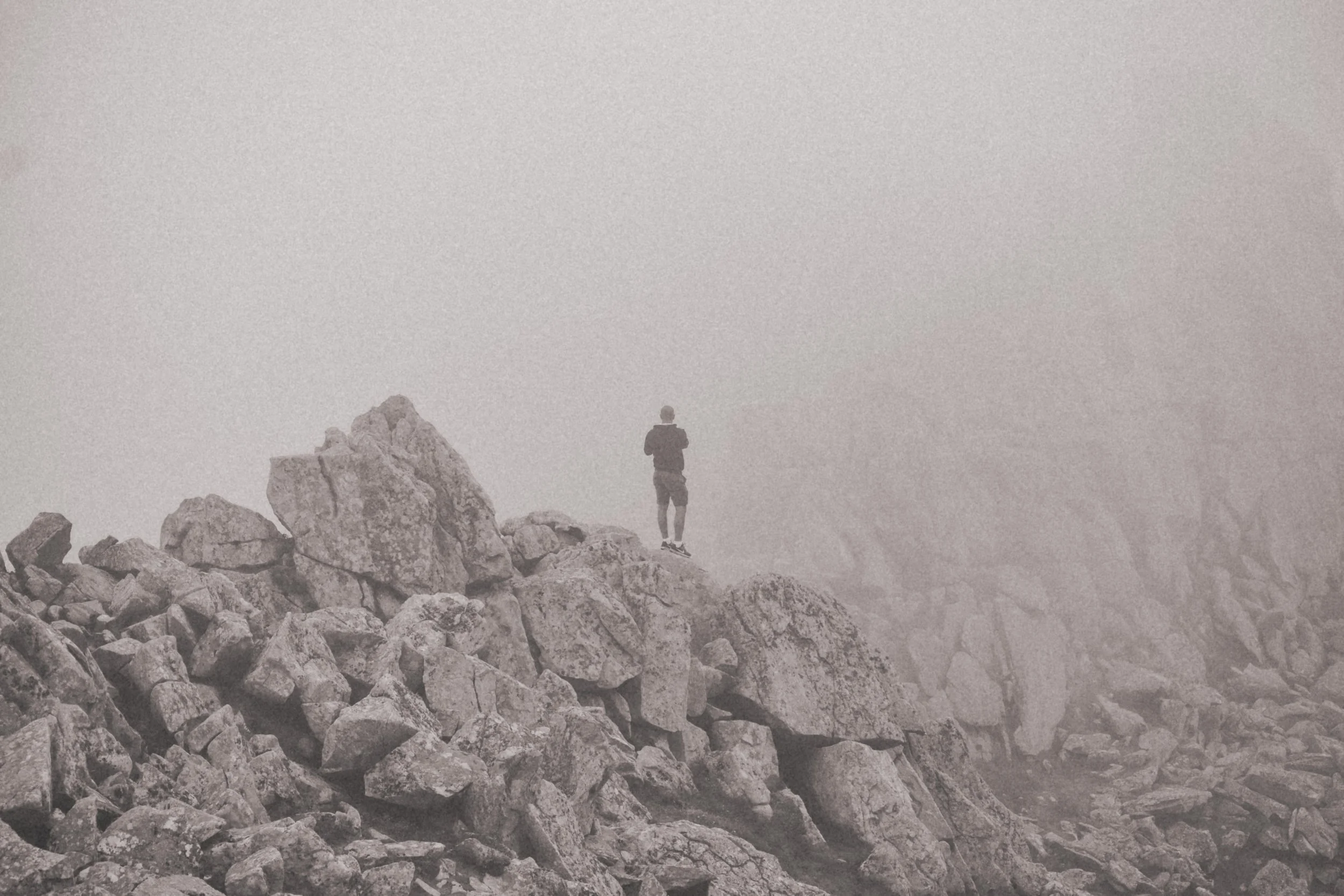Une personne debout sur des rochers dans une atmosphère brumeuse, regardant au loin.