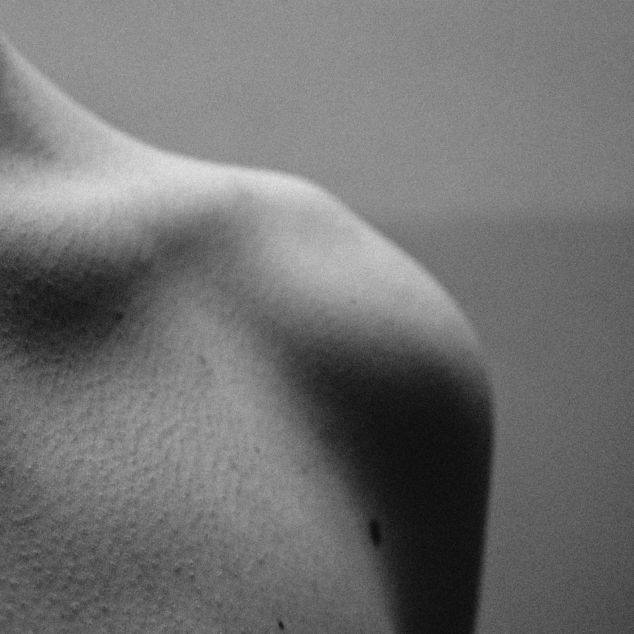 Une photographie en noir et blanc d'une zone du corps humain, probablement le bras ou la main, vue en gros plan avec une texture de la peau visible.