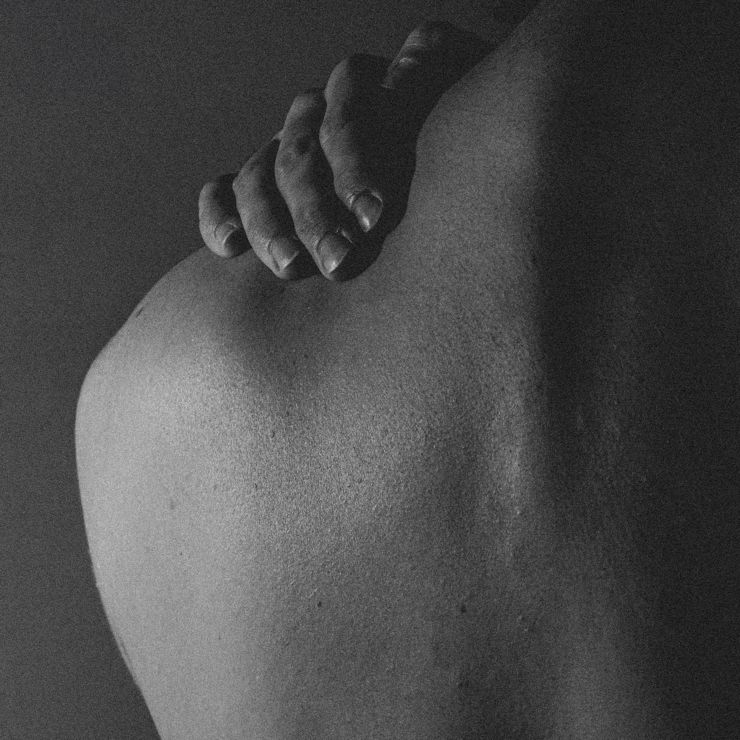 Une main noire posée sur la nuque d'une personne nue, en noir et blanc.