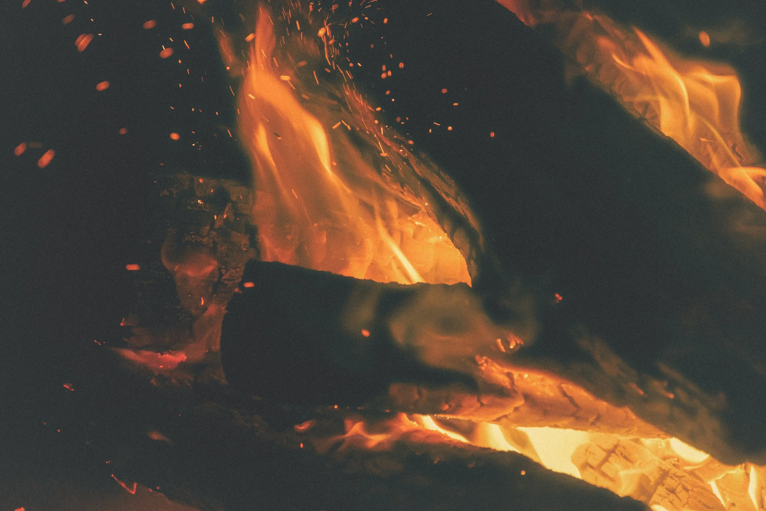 Un feu de bois en combustion avec des flammes orange et des étincelles brillantes, illuminant la scène sombre.