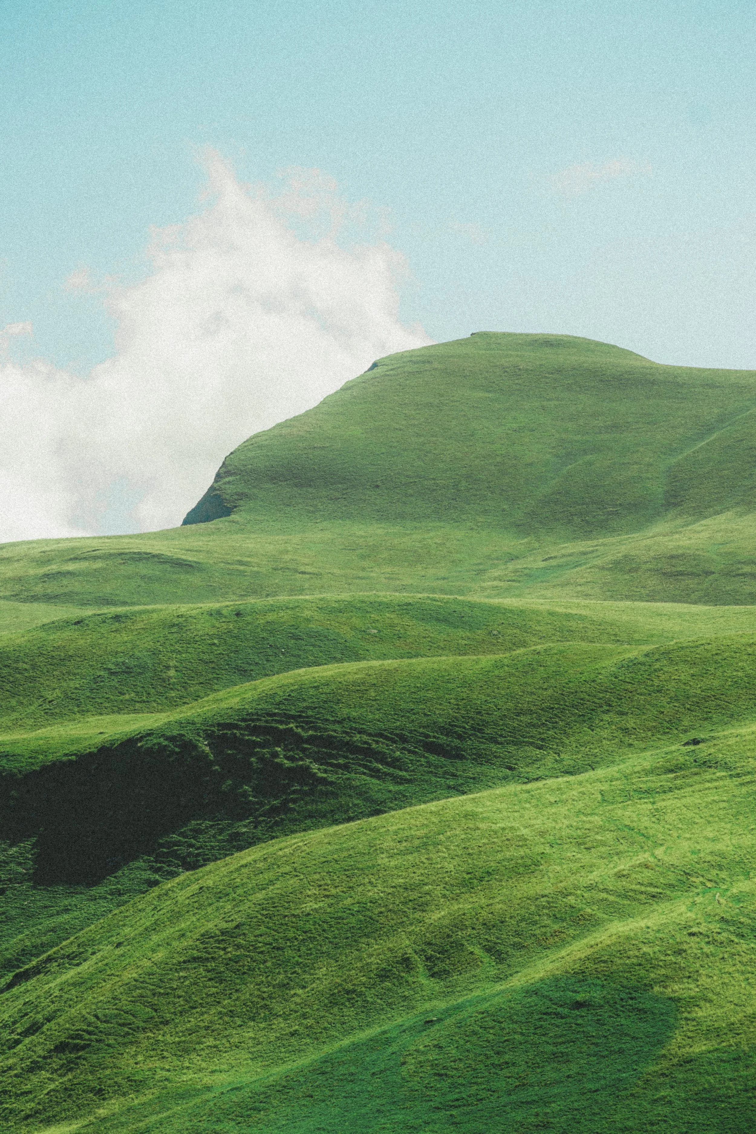 Collines verdoyantes sous un ciel bleu avec quelques nuages blancs.