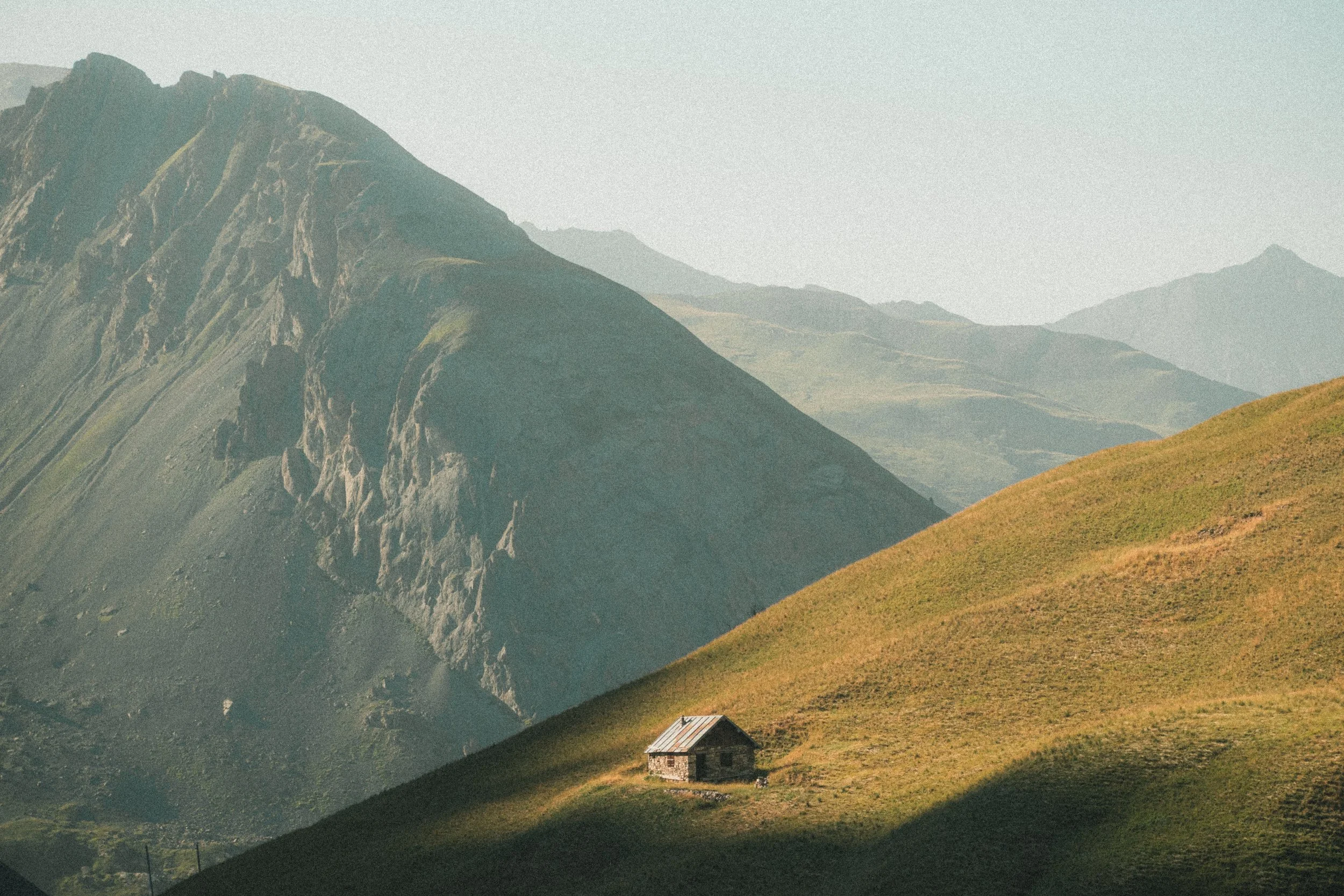 Petite cabane en bois au milieu d'une colline verdoyante avec des montagnes en arrière-plan.