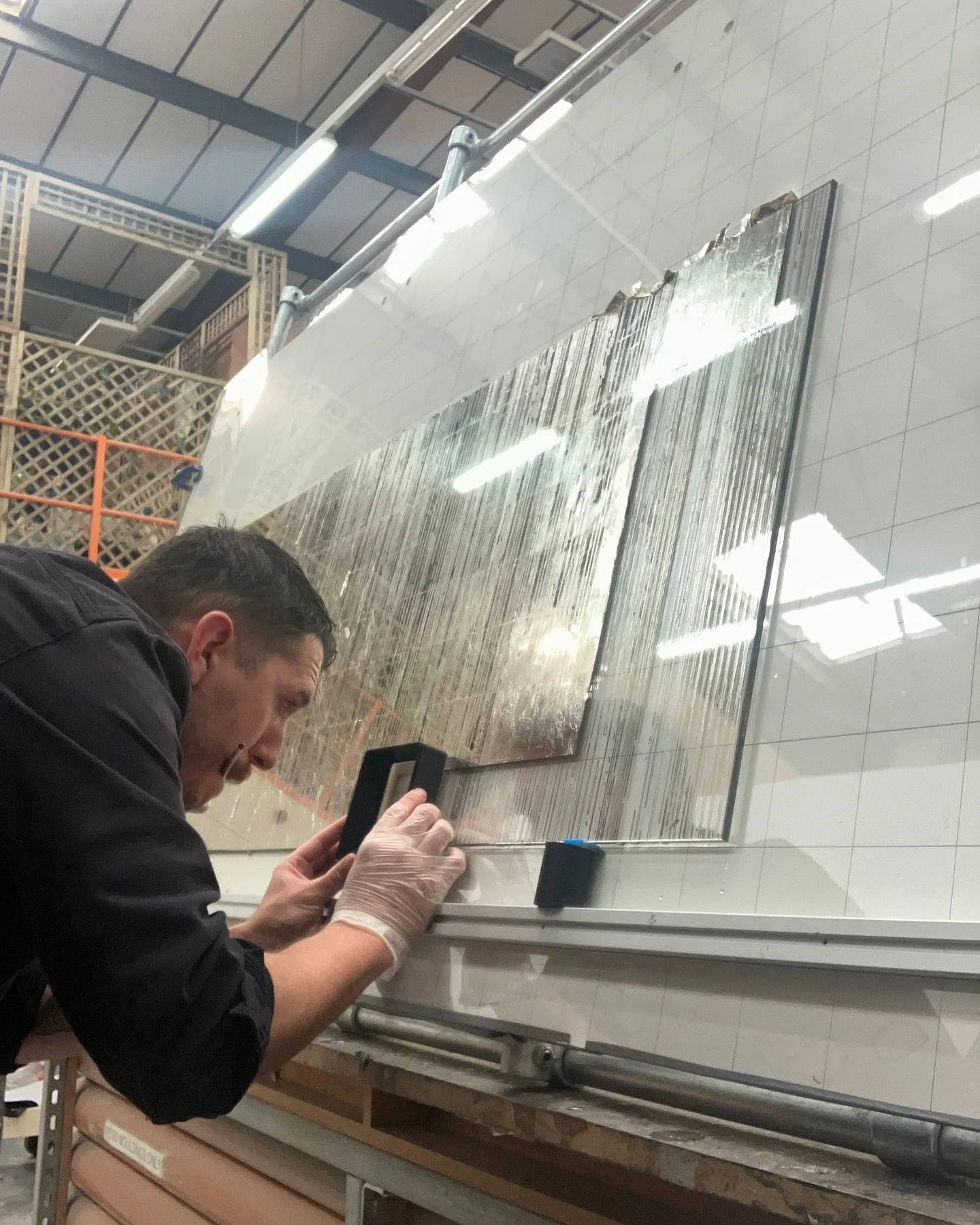 More large decorative panel gilding with platinum leaf at Stirling Studios. Each panel is gilded, then textured/backed-up to lock in the metal before rubbing areas back to reveal the pattern. The glass is then re-gilded, starting from different point
