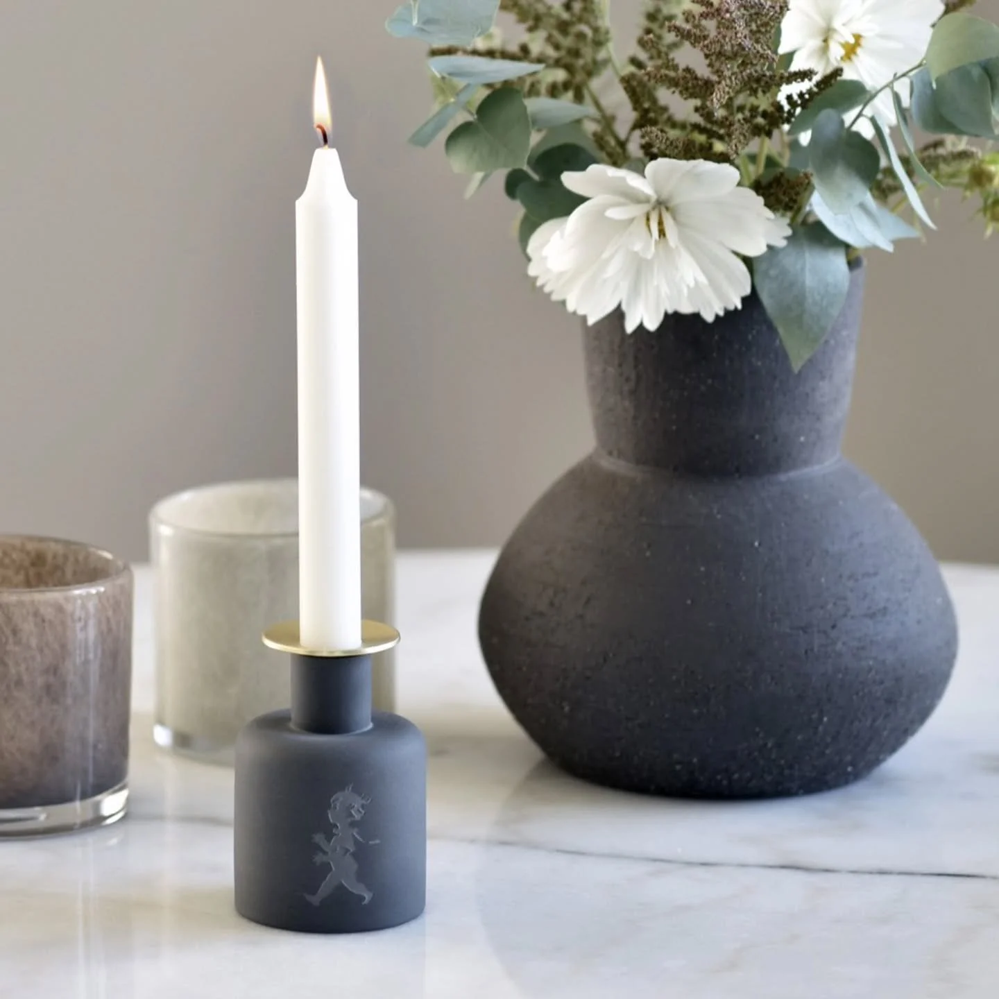 Stilren ljusstake i keramik som kombinerar form och funktion.

Med den medf&ouml;ljande ljusmanschetten i guld skyddas underlaget fr&aring;n stearin. En vacker inredningsdetalj f&ouml;r b&aring;de vardag och festdukning🖤