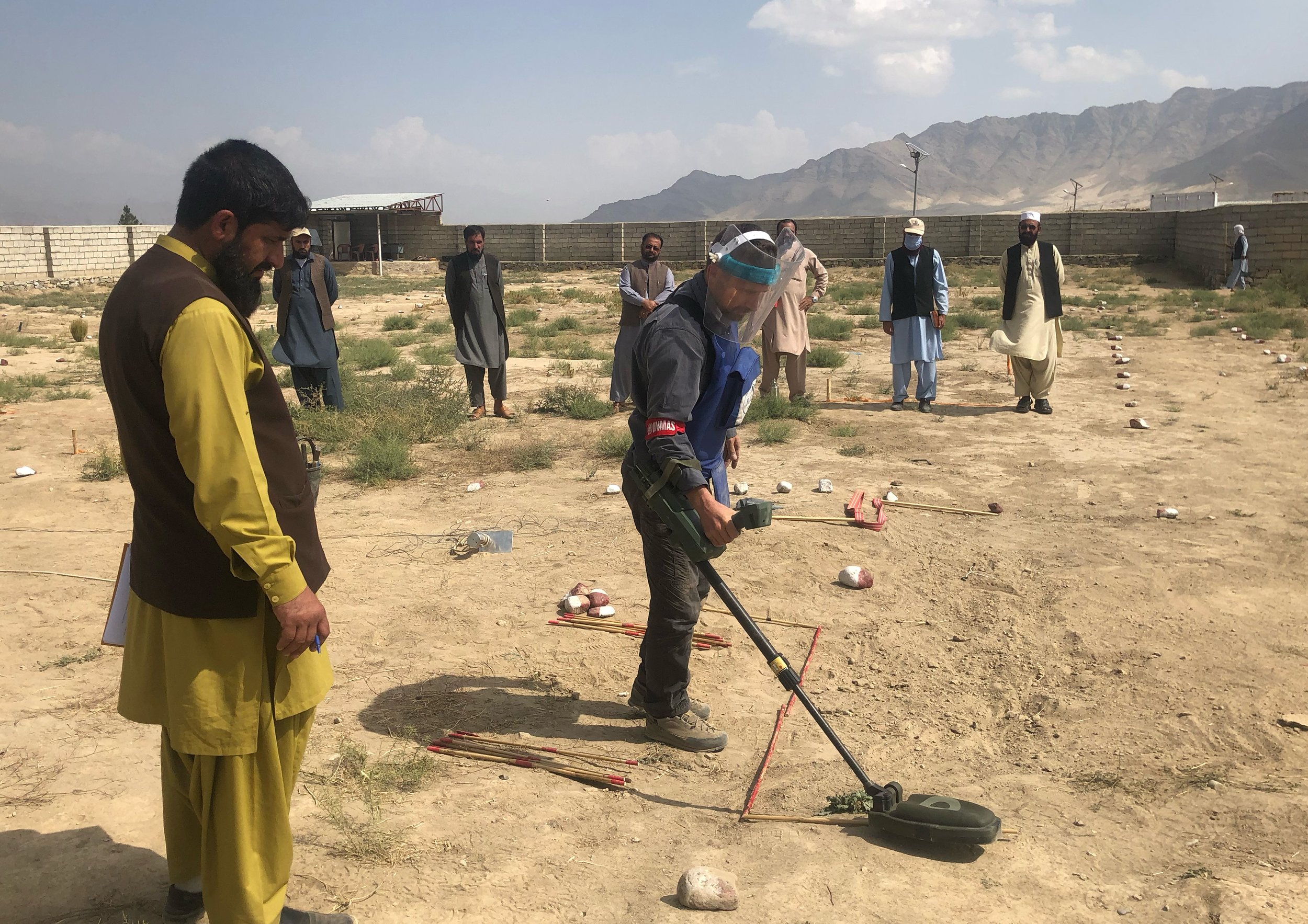  A group of trainees, with a supervisor overseeing, conduct a practical mine detection exercise, showcasing a collaborative training environment essential for effective UXO risk mitigation. 