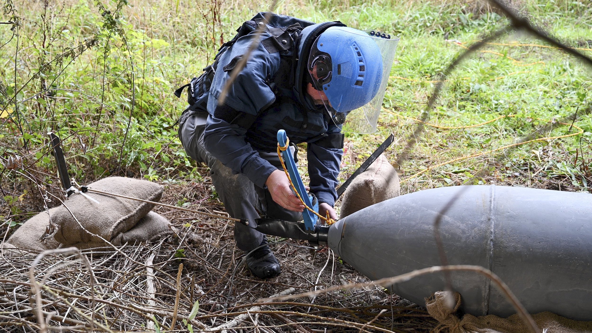  A technician in protective gear examines a large piece of ordnance, demonstrating the hands-on aspect of Artios Global’s training in ordnance identification and disposal. 