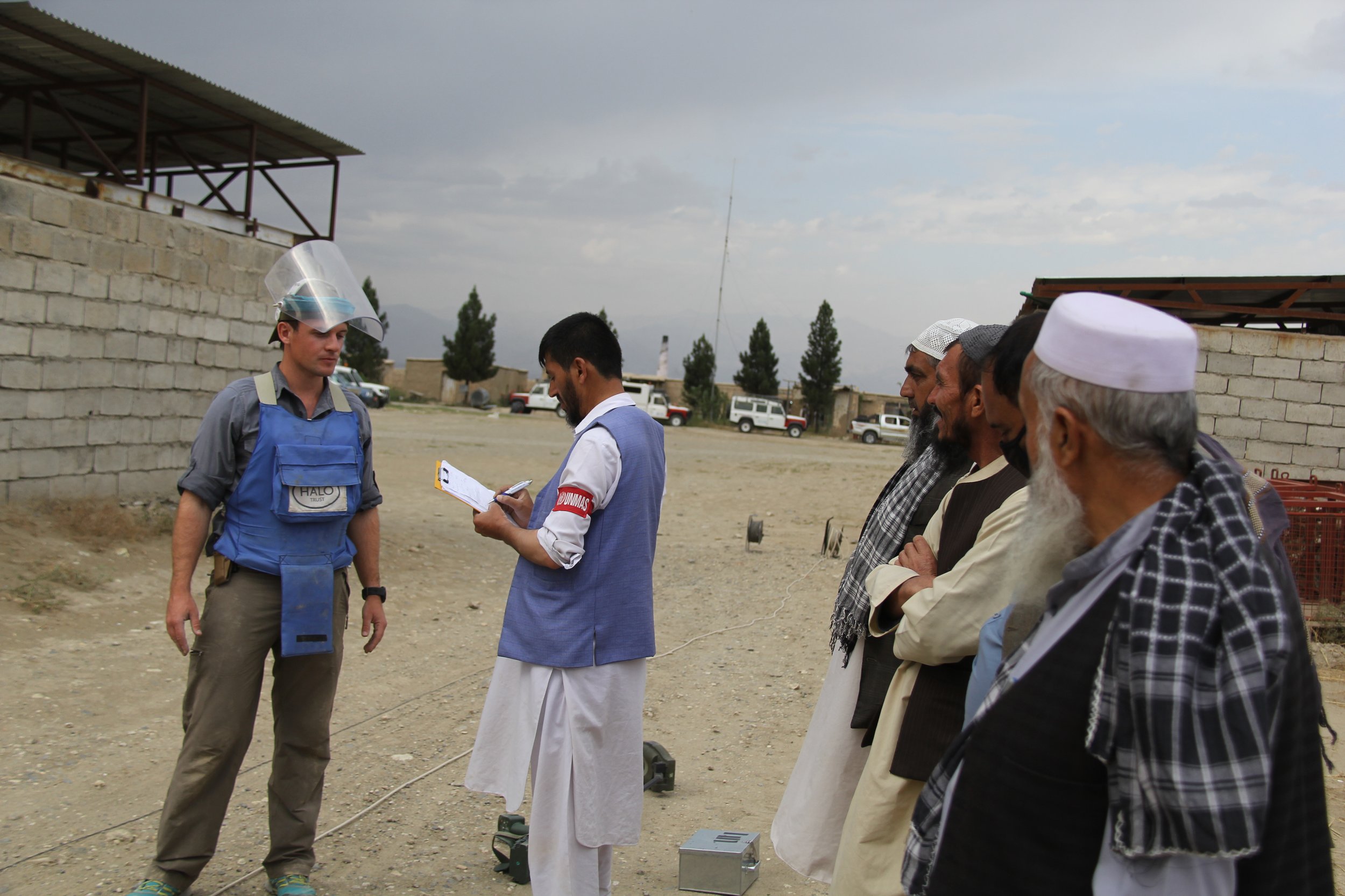  Individuals in a field setting engage in a discussion,  part of an Artios Global training session focused on Explosive Ordnance Disposal (EOD) and related mine action topics. 