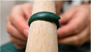Smooth green wax ring being checked for size on a wooden ring mandrel.