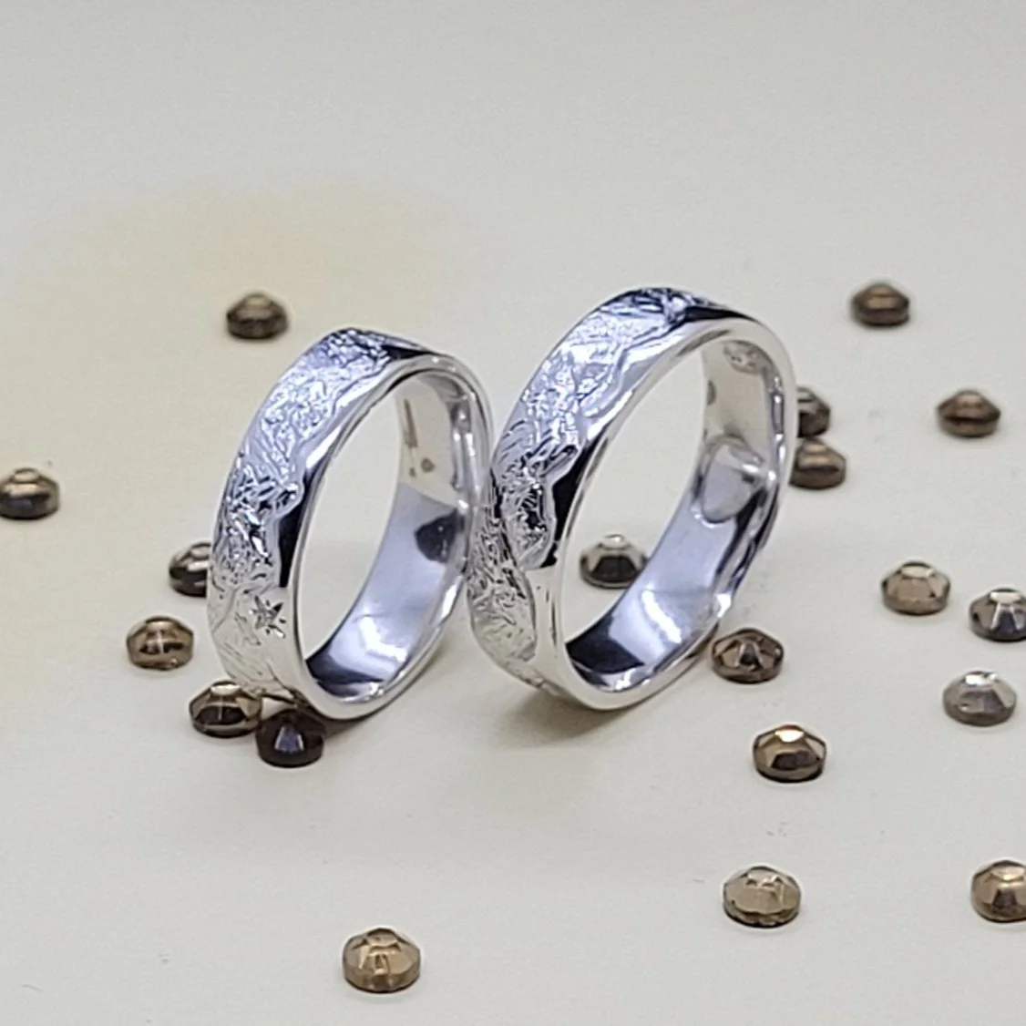 Two 18ct white gold wedding bands with engraved mountain patterns on a light surface, surrounded by scattered small diamonds .