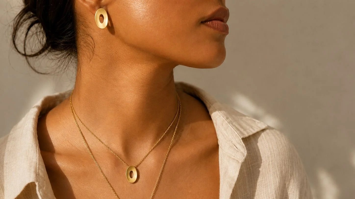 Model wearing layered gold Floating Ovals necklaces and matching oval stud earring, showcasing the concave sculptural design in warm natural light.