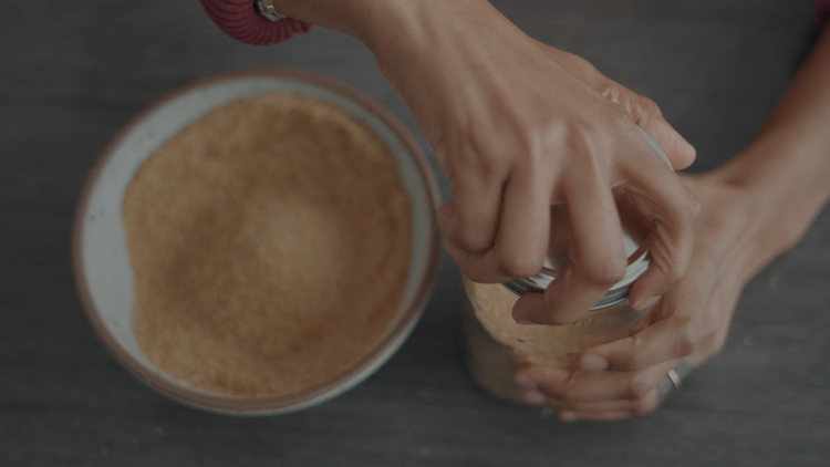 Close-up of Yasmin Cheyenne with a bowl of brown sugar and her hands opening a jar.