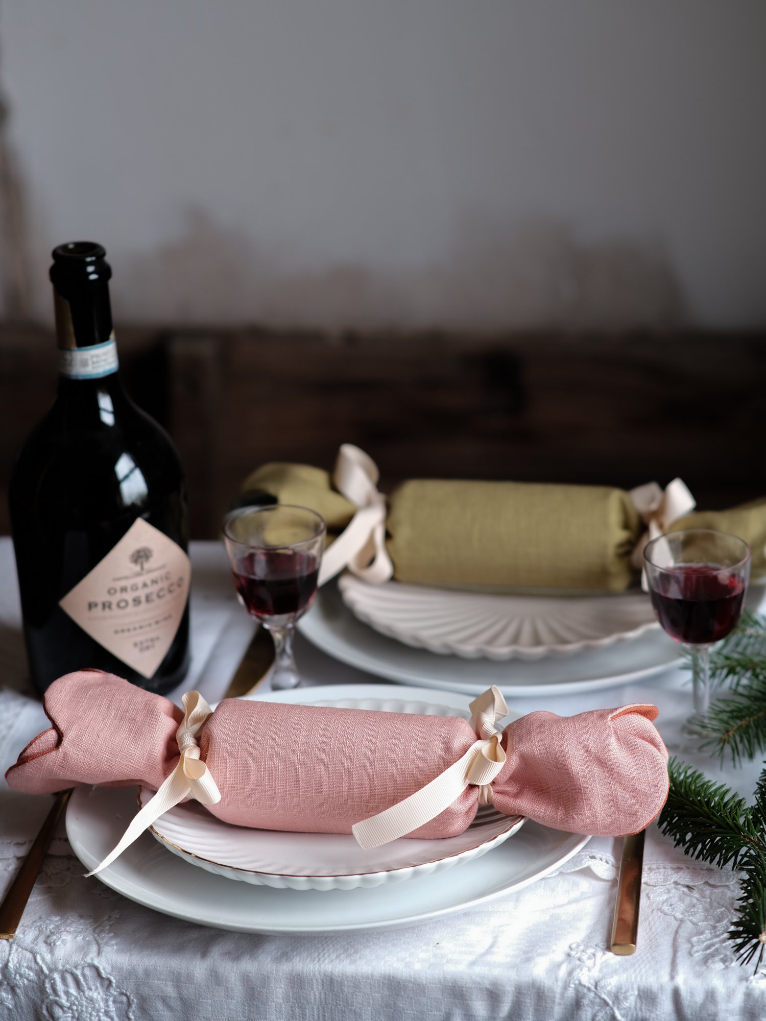 Reversible reusable linen Christmas crackers in soft pink, sage green, cream and muted festive colours, tied with natural ribbon and arranged on a family Christmas table