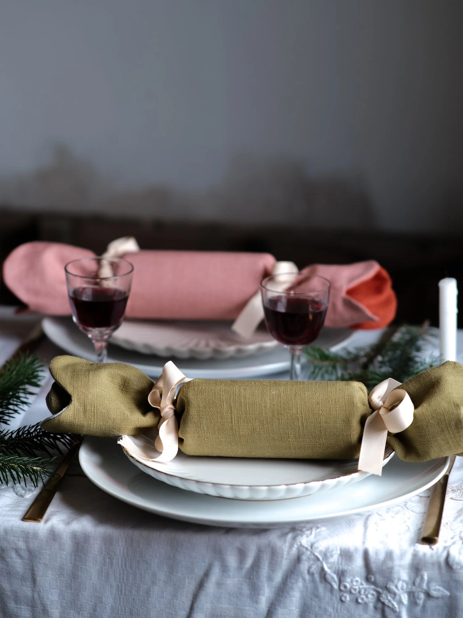 Reversible reusable linen Christmas crackers in soft pink, sage green, cream and muted festive colours, tied with natural ribbon and arranged on a family Christmas table