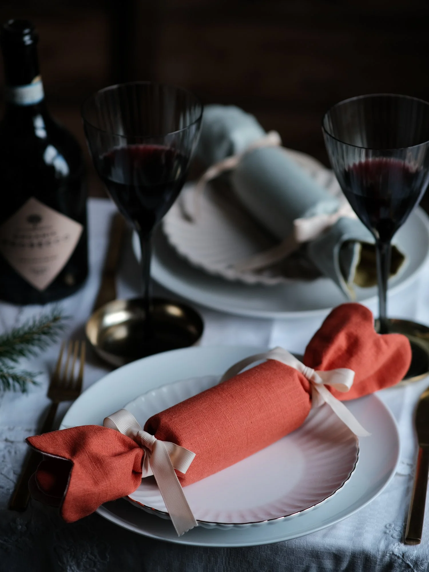 Reversible reusable linen Christmas crackers in soft pink, sage green, cream and muted festive colours, tied with natural ribbon and arranged on a family Christmas table