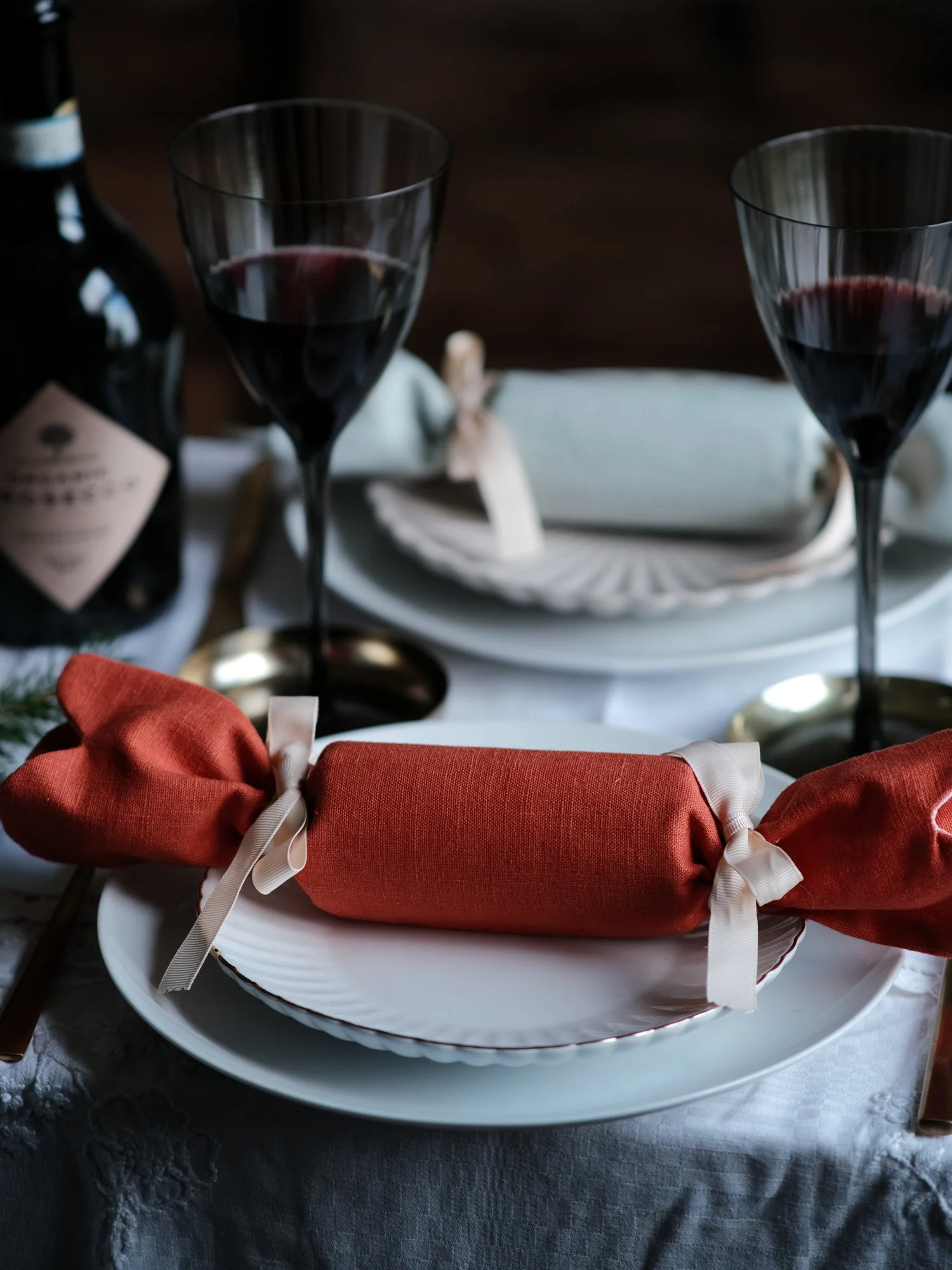 Reversible reusable linen Christmas crackers in soft pink, sage green, cream and muted festive colours, tied with natural ribbon and arranged on a family Christmas table