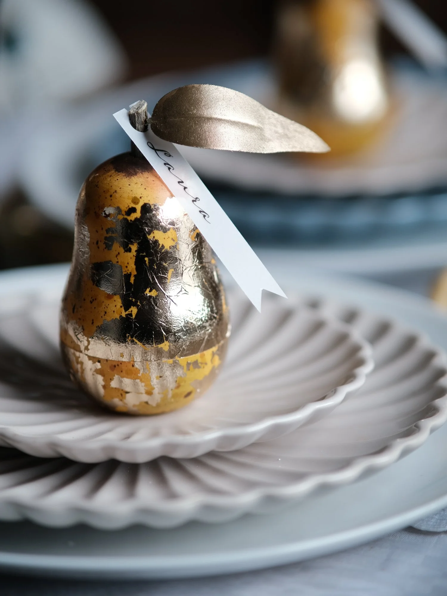 Gilded vintage-style Christmas pear ornament opened to reveal a small surprise inside, shown on a festive Christmas table setting with white plates and ribbon.