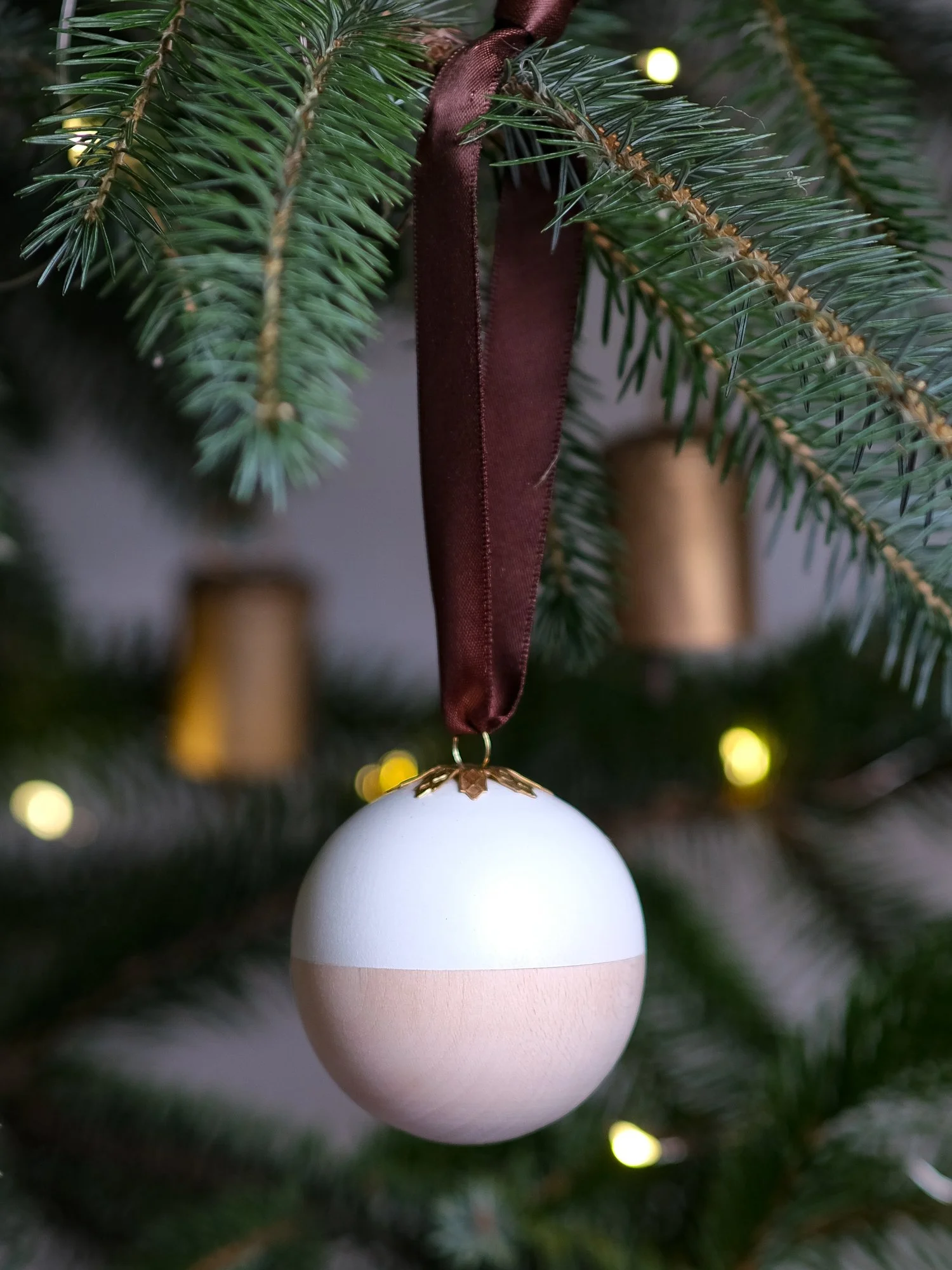 Wooden and white Christmas gift bauble with a removable lid, hanging from a Christmas tree with a space inside for a handwritten message, gift or surprise.
