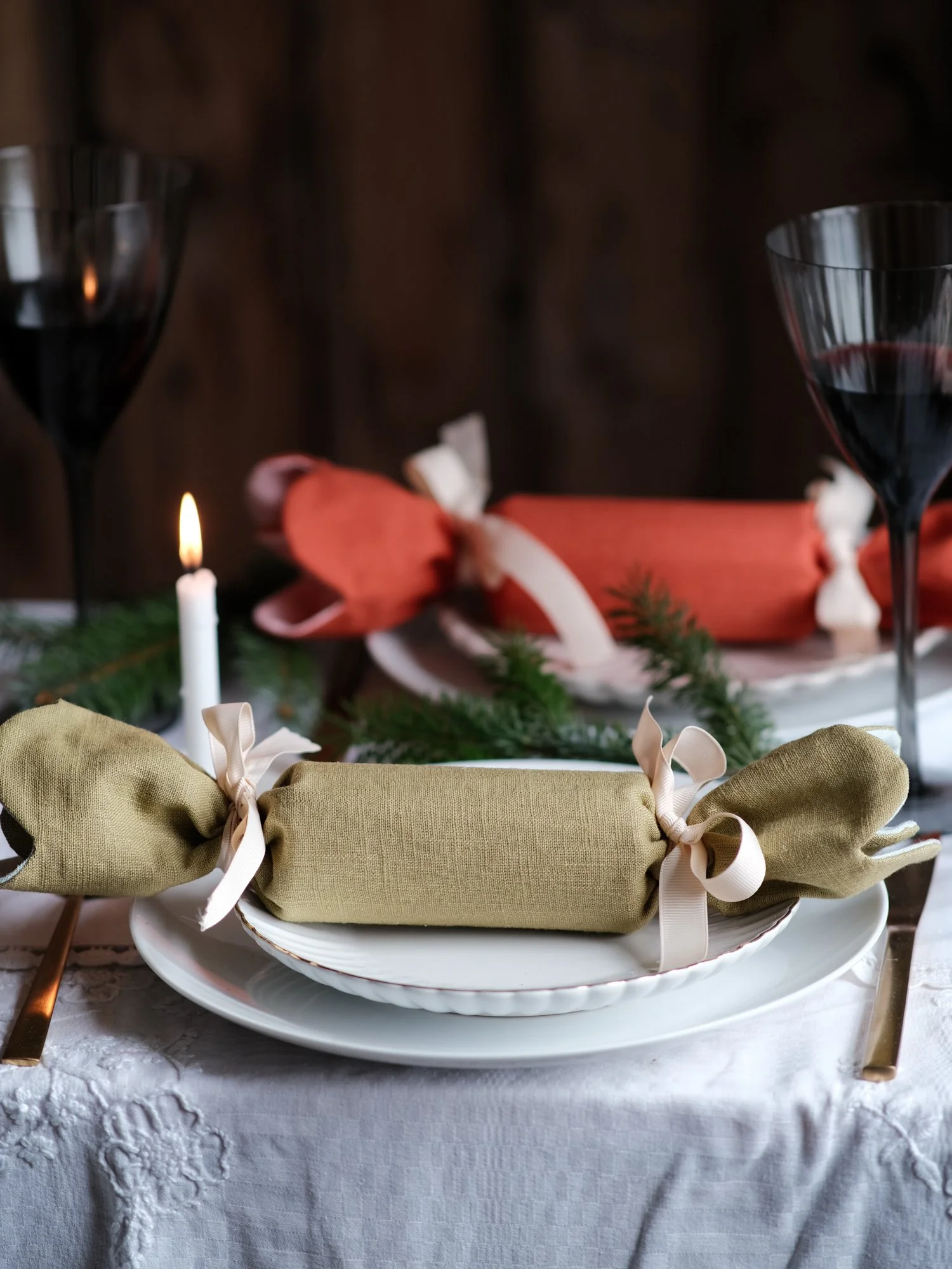 Reversible reusable linen Christmas crackers in soft pink, sage green, cream and muted festive colours, tied with natural ribbon and arranged on a family Christmas table