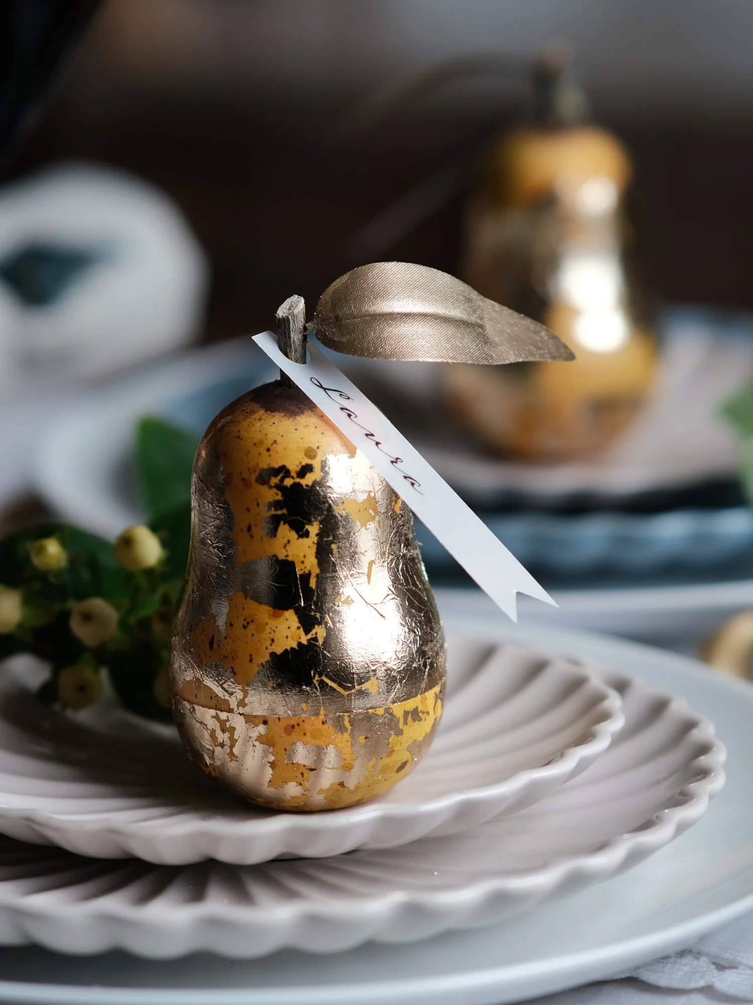 Gilded vintage-style Christmas pear ornament opened to reveal a small surprise inside, shown on a festive Christmas table setting with white plates and ribbon.