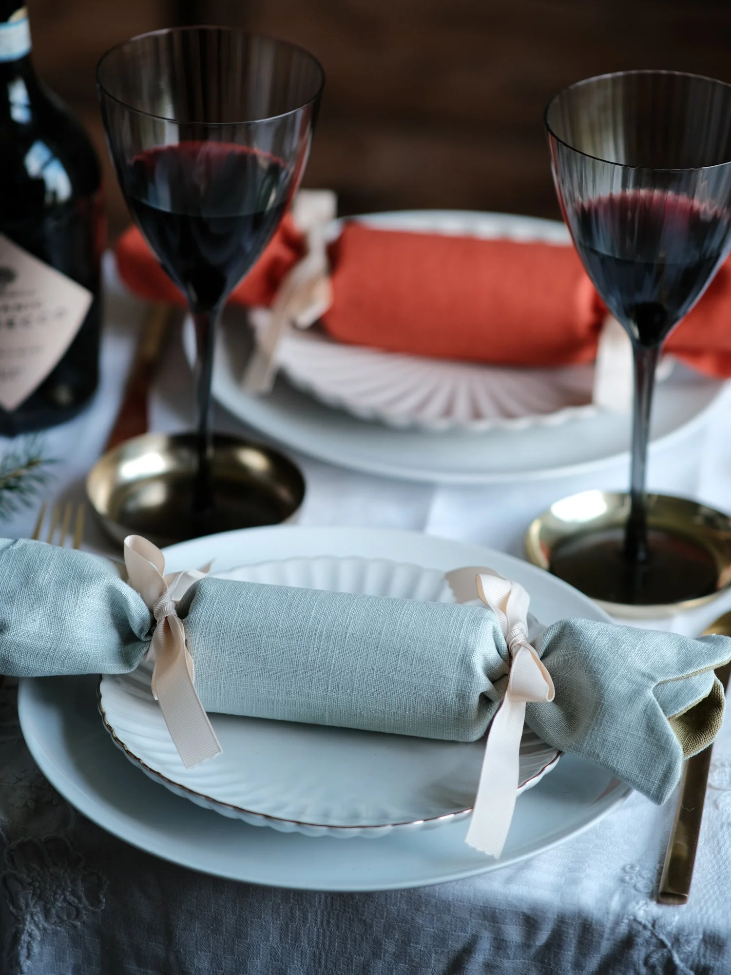 Reversible reusable linen Christmas crackers in soft pink, sage green, cream and muted festive colours, tied with natural ribbon and arranged on a family Christmas table