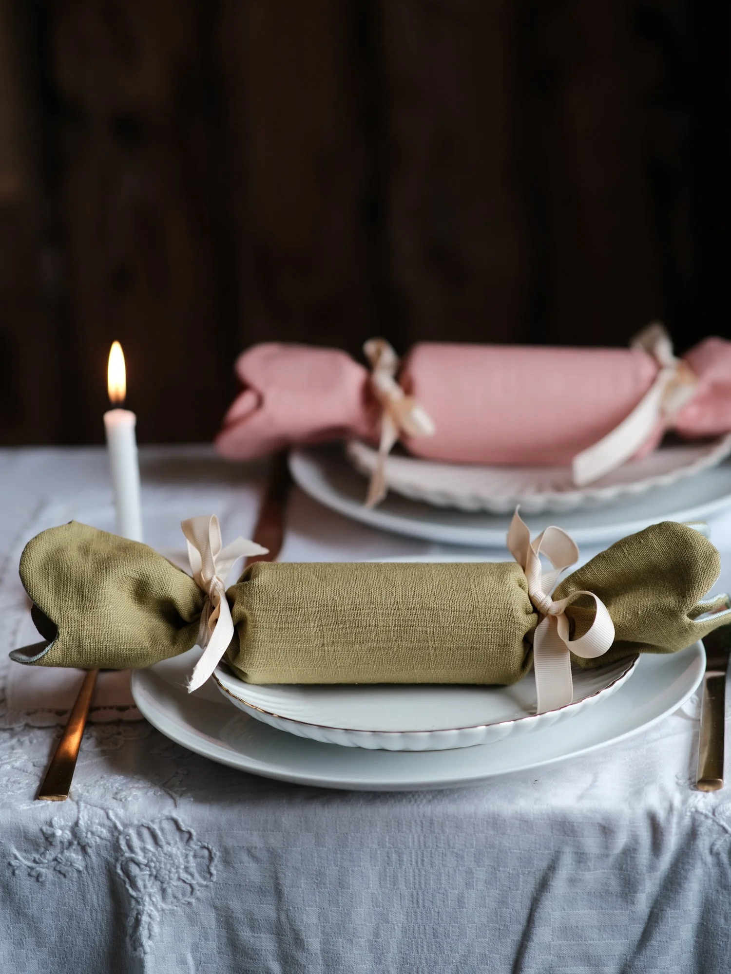 Reversible reusable linen Christmas crackers in soft pink, sage green, cream and muted festive colours, tied with natural ribbon and arranged on a family Christmas table