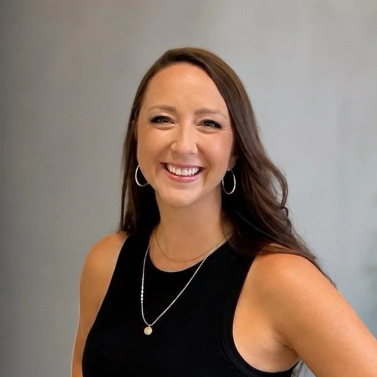 Woman with brown hair, hoop earrings, and a necklace in a black shirt smiles at the camera