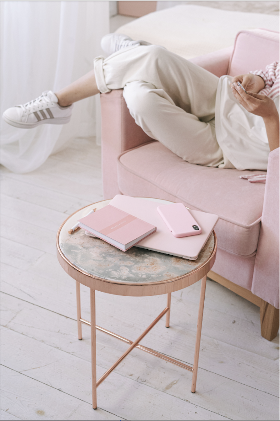 A person relaxing on a pink sofa with a journal and phone on a side table, representing a calm and low-pressure environment for executive functioning coaching and skill building.