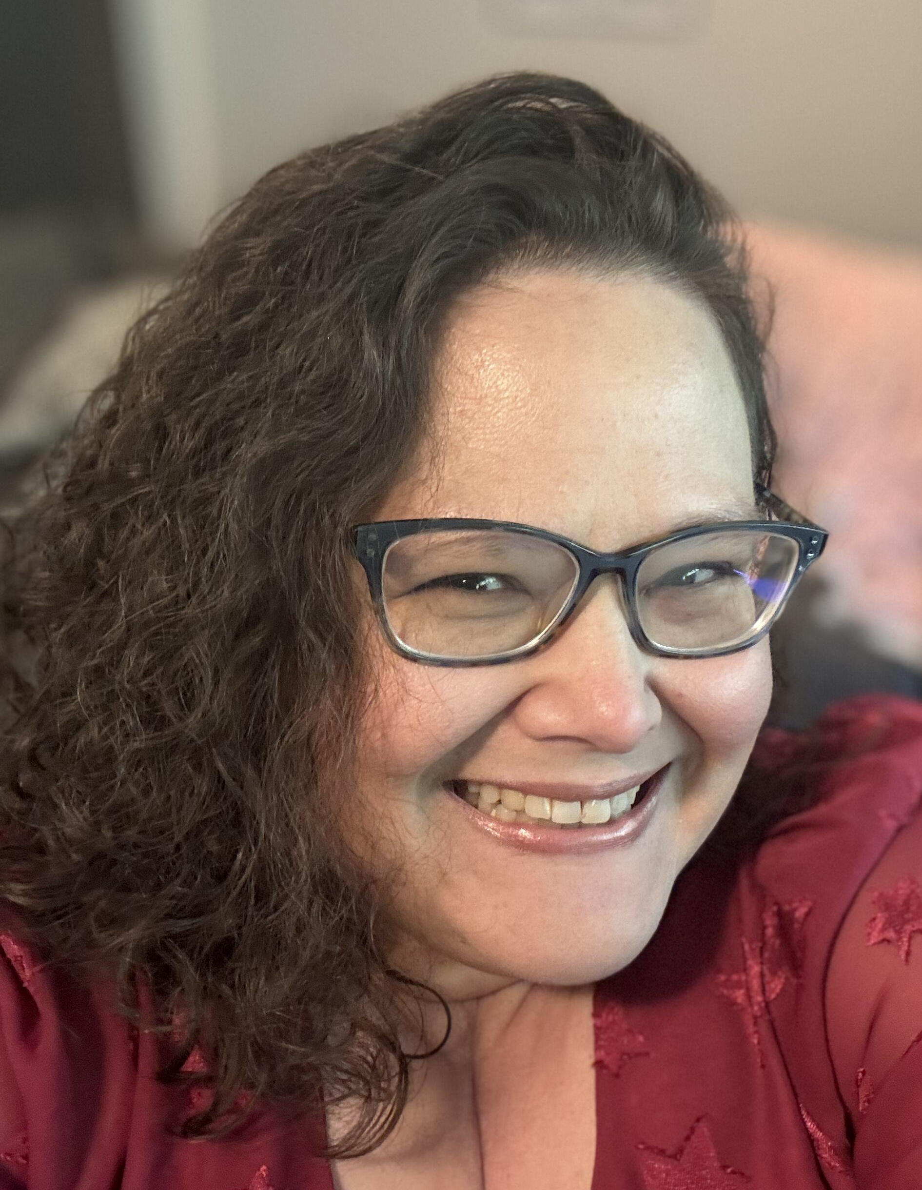 Woman with curly brown hair with glasses smiling at the camera