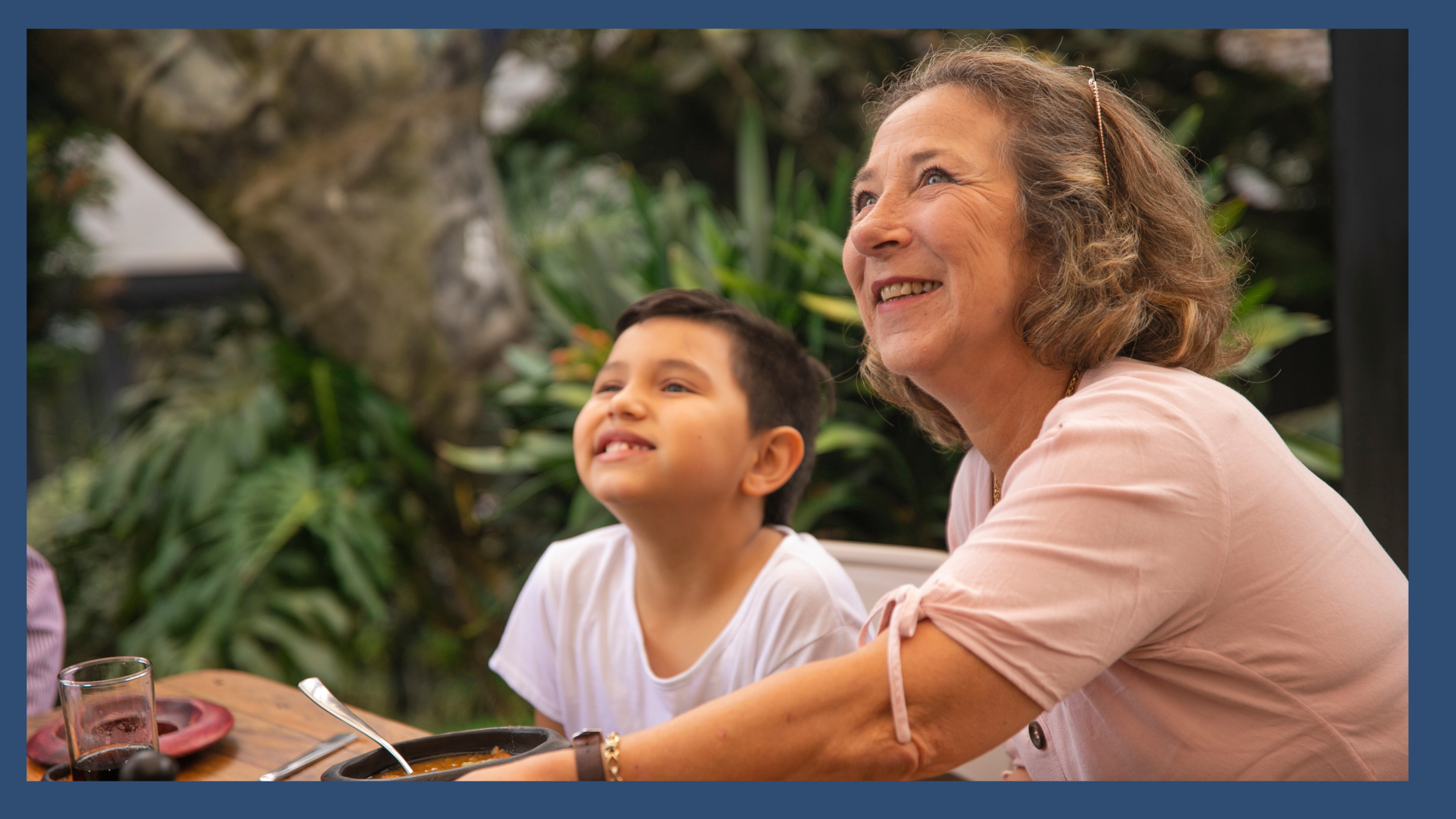 A grandmother and young child smiling together at an outdoor table, representing joyful connection and the real-life summer moments that build executive functioning and planning skills